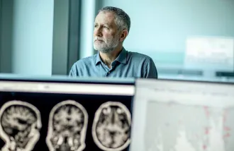 Michael Greicius stands behind computer screens displaying brain scans and text.