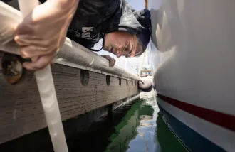 A person in a wet suit peers over the side of a dingy.